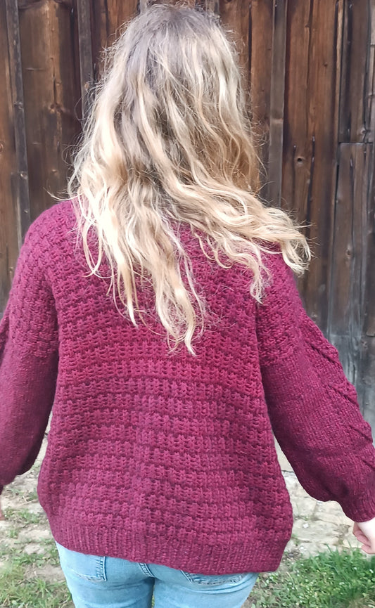 Lisa steht mit dem Rücken zum Betrachter vor einem Holztor. Sie trägt Jeans und den weinroten Cardigan. Ihre Haare fallen offen über den Rücken und sie breitet die Arme leicht aus. Mittig am Rücken ist eine hellere Stelle im Garn zu sehen.