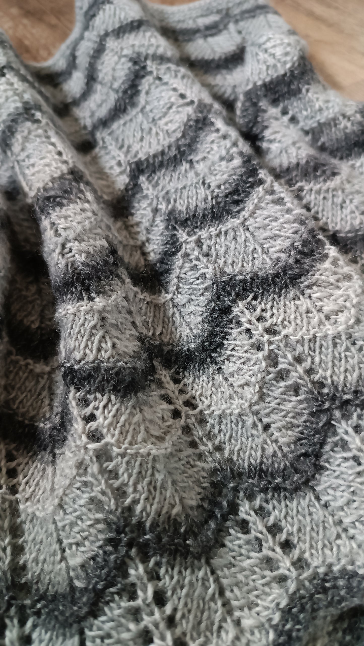 Nahaufnahme des grauen Cowls, auf dem Boden liegend. Das Wellenmuster aus hell- und dunkelgrau sowie die Lochmuster-Streifen sind gut zu sehen.