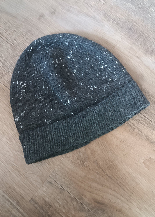 Eine anthrazit-farbene Beanie mit Tweed-Noppen liegt schräg im Bild, das Rippenbündchen nach unten geklappt.