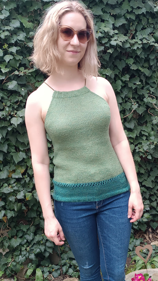 Lisa steht vor einer Efeuwand und trägt ein Neckholder-Top. Es ist olivgrün bis zum oberen Rand der Hüfte, darunter schließt sich ein petrol Streifen an. Dazu trägt sie eine dunkelblaue Jeans.