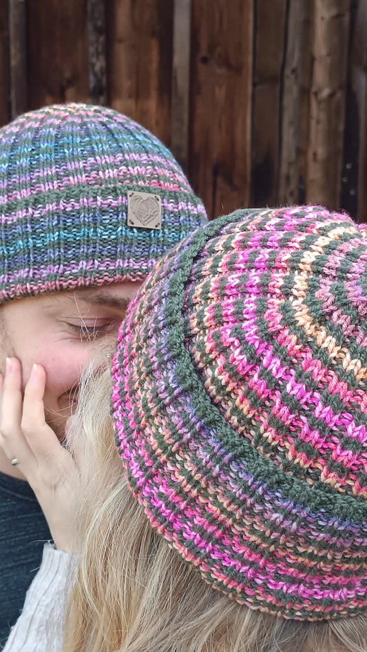 Lisa und Andreas stehen sich gegenüber, Lisa mit dem Rücken zur Kamera und der Hand auf Andreas Wange. Sie tragen die beiden Ringelmützen, Lisa die rosa Variante, Andreas die blaue.